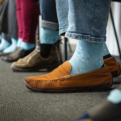 A row of people seated in chairs wearing matching blue socks featuring an isotope pattern.