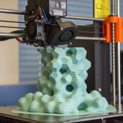 A 3D printer creates an abstract shape from light green material, starting out with soft, round edges that gradually become sharper and more defined.