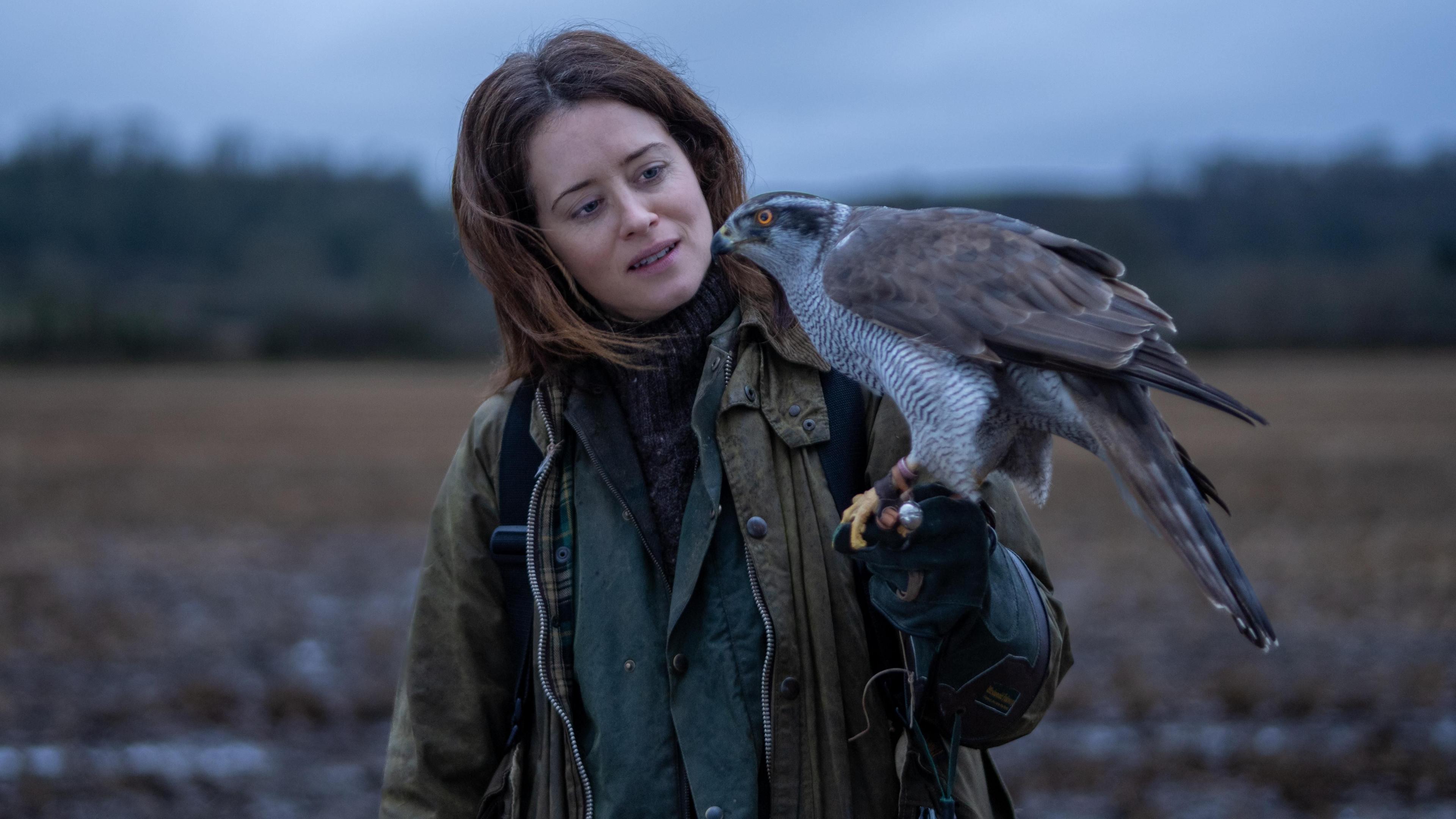a woman stands in a field with a hawk on her arm