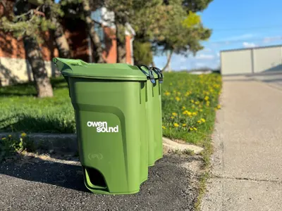 Two green bins sitting at end of driveway, above sidewalk