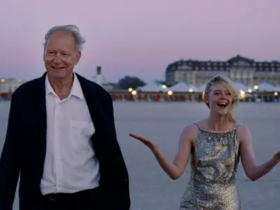 older man and younger woman in dress clothes walking in front of a hotel on a beach