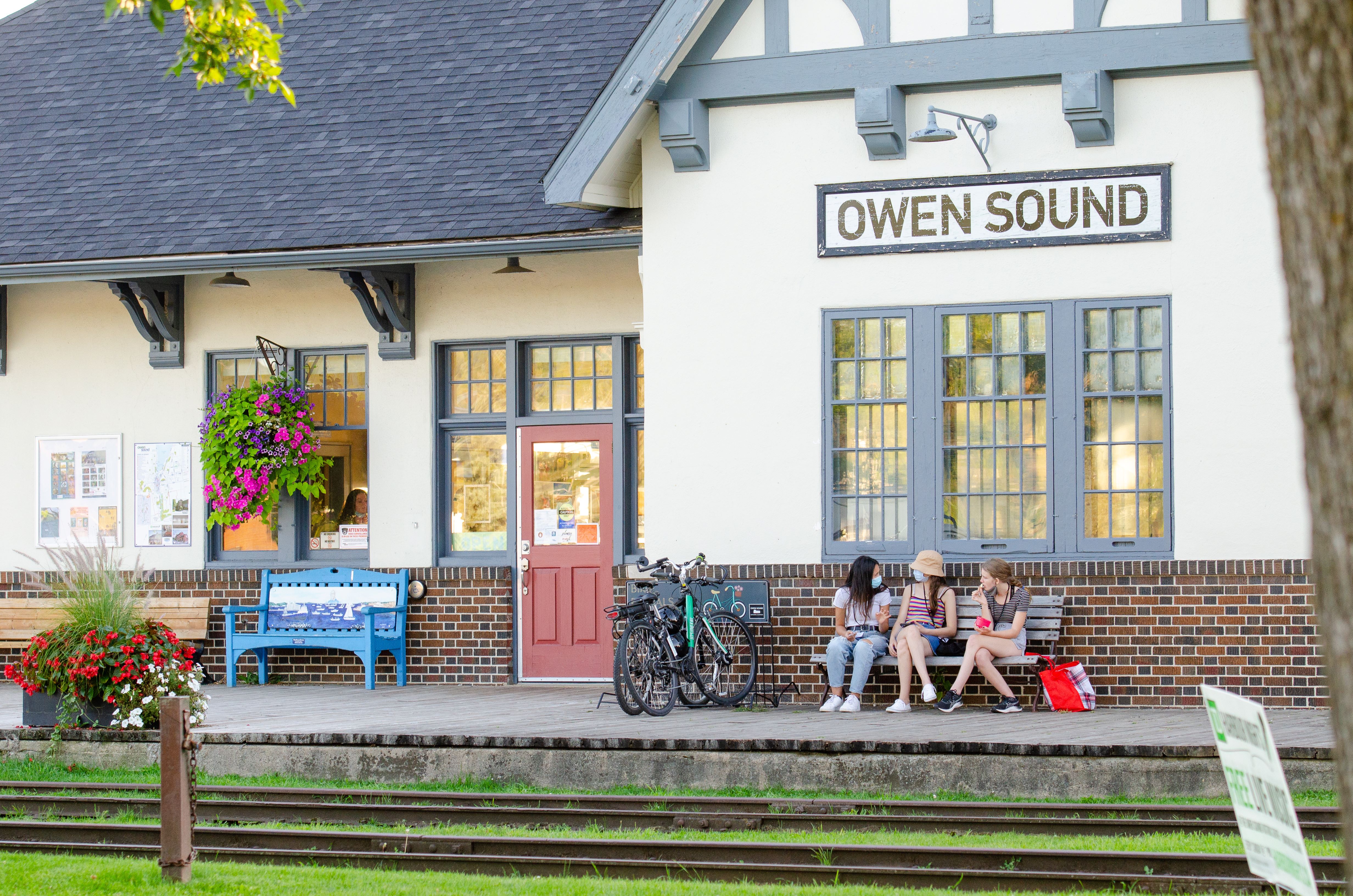 People sitting on bench in front of Owen Sound rail museum building
