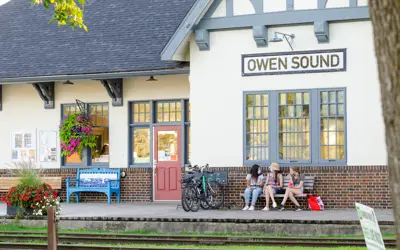 People sitting on bench in front of Owen Sound rail museum building